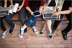 Students using devices sitting on a bench.