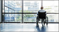 Man in wheelchair looking out a glass wall of windows